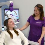 Woman receiving NeuroStar TMS therapy, seated with coil positioned over her head as a clinician assists.